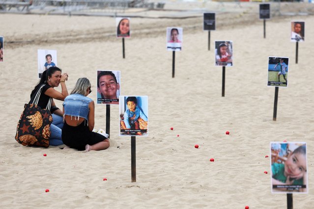 Vanessa Freitas Moreira sits next to her son Joao Vitor Moreira dos Santos's photo, during a demonstration of NGO Rio de Paz displaying pictures of children who were shot dead during police operations during the administration of Rio de Janeiro's governor Claudio Castro, at Copacabana beach in Rio de Janeiro, Brazil on December 18, 2024. (Photo by Pilar Olivares/Reuters)