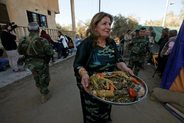 A woman carries a platter of Dolma, a traditional Iraqi dish, before giving it to Peshmerga forces in the town of Bashiqa after the town was recaptured from the Islamic State, east of Mosul, Iraq, November 19, 2016. (Photo by Azad Lashkari/Reuters)