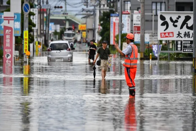 Residents manoeuver through a flooded street in the city of Kureme, Fukuoka prefecture, on July 10, 2023, after heavy rains hit wide areas of Kyushu island. (Photo by Kazuhiro Nogi/AFP Photo)