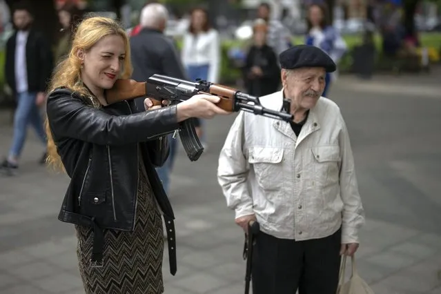 A woman uses a plastic Kalashnikov rifle to shoot balls at a portrait of Russian President Vladimir Putin, at a street attraction in the centre of Lviv, Ukraine on Saturday, May 14, 2022. (Photo by Emilio Morenatti/AP Photo)
