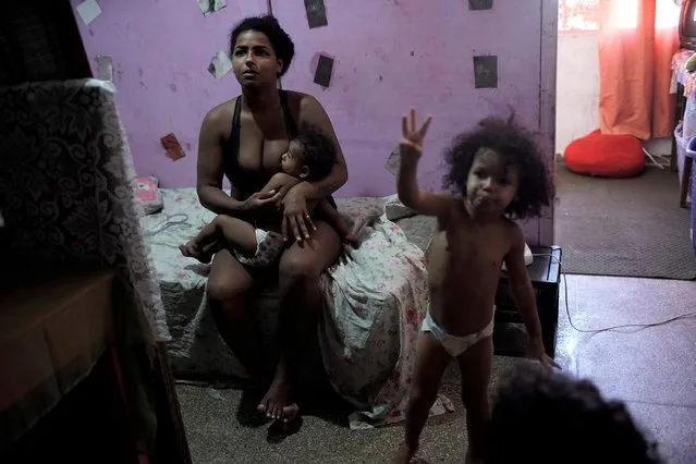 Thayane, who used to make a living as a manicurist, breastfeeds her one-year-old daughter Mirella in their room of an occupied building where she lives with her three daughters, in Rio de Janeiro, Brazil, Thursday, March 11, 2021. Before the coronavirus pandemic hit Thayane had steady work as a manicurist, riding her bike to clients’ homes or receiving walk-ins at the squat. (Photo by Silvia Izquierdo/AP Photo)