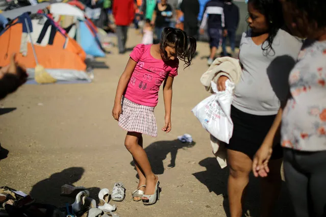 A girl tries on shoes as she waits with members of a caravan from Central America, who are trying to reach the United States, in a temporary shelter in Tijuana, Mexico, November 24, 2018. (Photo by Lucy Nicholson/Reuters)