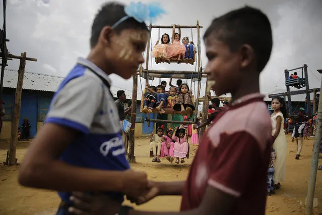 Rohingya refugee boys greet each other as girls ride in a ferris wheel, specially brought in to the camps for Eid al-Adha celebrations, at the Kutupalong refugee camp in Bangladesh, Wednesday, August 22, 2018. Hundreds of thousands of Rohingya refugees are celebrating the Feast of Sacrifice in sprawling Bangladeshi camps where they have been living amid uncertainty over their future after they fled Myanmar to escape violence. (Photo by Altaf Qadri/AP Photo)