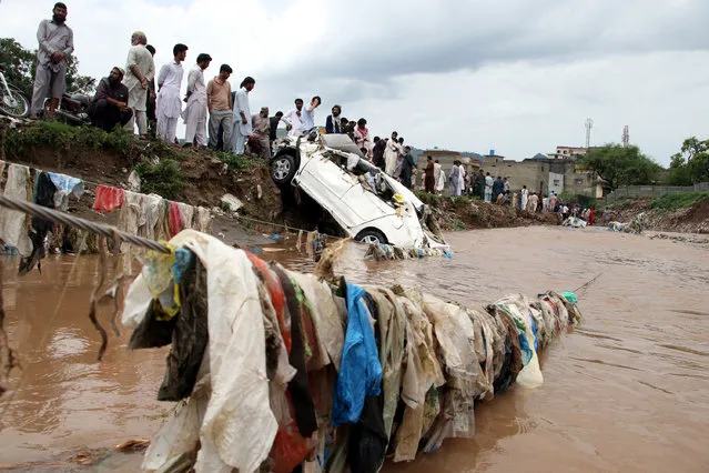 Vehicles and trash is seen washed away as a crowd of people watches rescue operations being carried out after floods that were caused by a cloud burst in Islamabad, Pakistan, 28 July 2021. Sector E 11 in Islamabad has been flooded with torrents that swept away cars and other vehicles after a hefty cloudburst. (Photo by Sohail Shahzad/EPA/EFE)