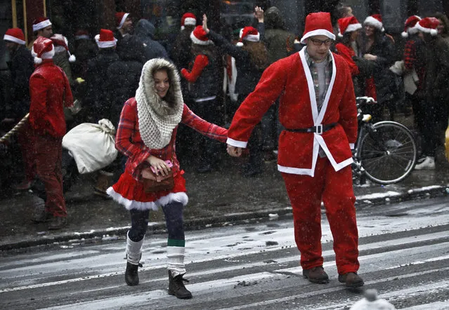 Snow falls as revelers dressed as Santa Claus walk in Manhattan during the annual SantaCon bar crawl event on December 14, 2013 in New York City. (Photo by Kena Betancur/Getty Images)