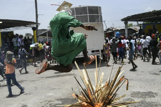 A person jumps over a bonfire on the street as members of the gang led by Jimmy Cherizier, alias Barbecue, a former police officer who heads a gang coalition known as “G9 Family and Allies”, march to demand justice for slain Haitian President Jovenel Moise in La Saline neighborhood of Port-au-Prince, Haiti, Monday, July 26, 2021. Moise was assassinated on July 7 at his home. (Photo by Matias Delacroix/AP Photo)