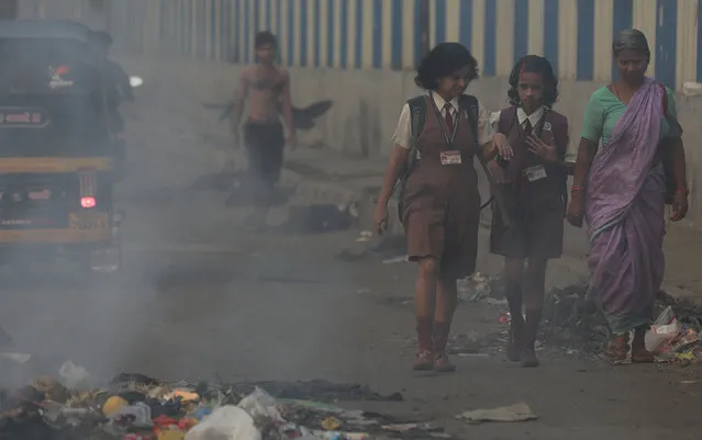 Schoolgirls walk past a burning garbage dump in Mumbai, India, Thursday, April 9, 2015. Air pollution kills millions of people every year, including more than 627,000 in India, according to the World Health Organization. The WHO puts 13 Indian cities in the world's 20 most polluted. (Photo by Rafiq Maqbool/AP Photo)