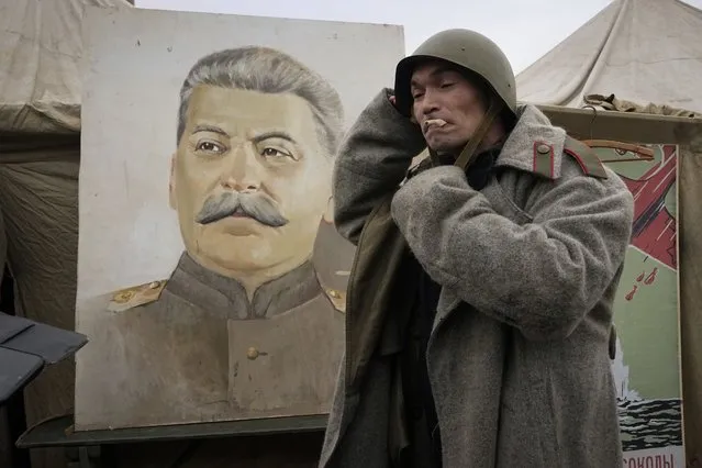 A man wears World War II ages Soviet Army's uniform near a portrait of Soviet dictator Josef Stalin at a military-historical exhibition at the Dvortsovaya (Palace) Square, in St. Petersburg, Russia, Saturday, January 27, 2024. (Photo by Dmitri Lovetsky/AP Photo)
