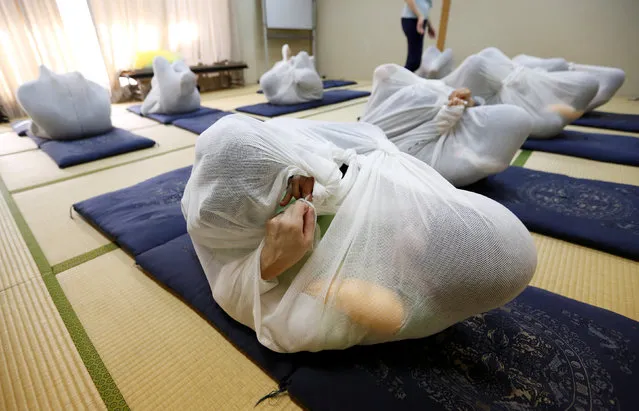 Participants perform Otonamaki, which translates as “adult wrapping”, a new form of therapy where people are wrapped in large swaddling cloth to alleviate posture problems and stiffness, at a session in Asaka, Saitama prefecture, Japan, February 4, 2017. Wrapped up from head to toe in a white bag and gently rocking from side to side, five Japanese mothers are hopeful Tokyo's latest health trend can cure their post-pregnancy aches and pains. According to its exponents, Otonamaki, which translates as “adult wrapping”, was devised by a Kyoto midwife who thought replicating how children are swaddled at birth could help mothers overcome post labor shoulder and hip pain. The five mothers at a recent session in Tokyo lay on their backs with their knees on their chests bundled up in white cloths. Staff then helped them rock over cushions. “It felt warm and there was this feeling with my body”, said one mother who tried the 20 minute session. “I have never experienced this before so its quite hard to describe properly”. Not everyone is a fan. Chiropractor Shiro Oba was skeptical about its powers of healing and encouraged mothers with back pain to visit a physician. “There may be cases where people with asthma may find it easier to breath (in that position), but once the cloth is off it's the same thing”, said Oba. “But apart from that, I just can't think of how people can benefit from this even as a form of reflexology or exercise”. (Photo by Toru Hanai/Reuters)
