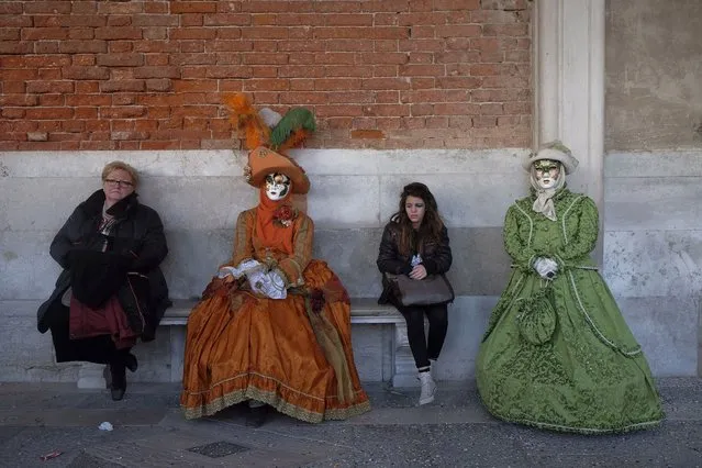 Tourists sit on a bench alongside masked revellers posing in Saint Mark's Square during the Venetian Carnival in Venice, on February 23, 2014. (Photo by Manuel Silvestri/Reuters)