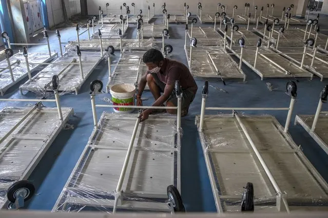 A workers installs a beds at a makeshift COVID-19 care center with 1200 beds in Mumbai, India, Friday, December 31, 2021. In India, millions of people were planning to ring in the new year from their homes, with nighttime curfews and other restrictions taking the fizz out of celebrations in large cities including New Delhi and Mumbai due to a surge of coronavirus infections, many infected with contagious omicron variant. (Photo by Rafiq Maqbool/AP Photo)