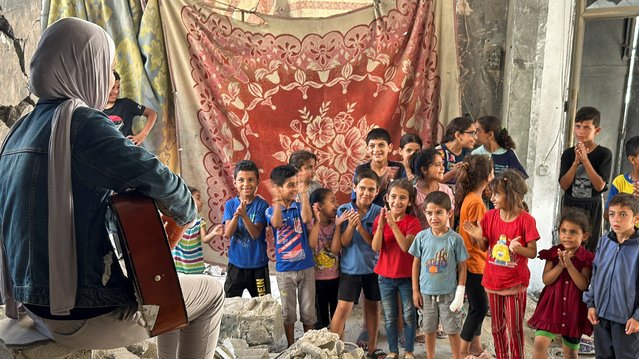 Children listen to a Palestinian medical student, Rahaf Nasser playing music, amid the ongoing conflict between Israel and Hamas, in Deir Al-Balah, in the central Gaza Strip on June 5, 2024. (Photo by Moaz Abu Taha/Reuters)