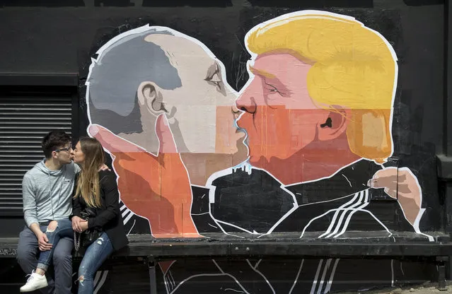 A couple kisses in front of graffiti depicting Russian President Vladimir Putin, left, and Republican presidential candidate Donald Trump, on the walls of a bar in the old town in Vilnius, Lithuania, Saturday, May 14, 2016. (Photo by Mindaugas Kulbis/AP Photo)
