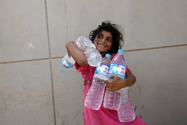 A girl smiles while holding water bottles she collected from a charity distribution point during a heatwave, outside the emergency department of Jinnah Postgraduate Medical Centre (JPMC) in Karachi, Pakistan, June 28, 2015. Sea breezes brought lower temperatures on Friday to ease a heat wave that killed more than 1,150 people around Pakistan's teeming port city of Karachi during the Muslim fasting month of Ramadan. (Photo by Akhtar Soomro/Reuters)
