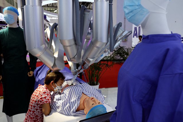 A child watches as a Shurui surgical robot, operated by a staff member (not pictured) from a console, performs “surgery” on a dummy at the World Robot Conference in Beijing, China on August 21, 2024. (Photo by Florence Lo/Reuters)