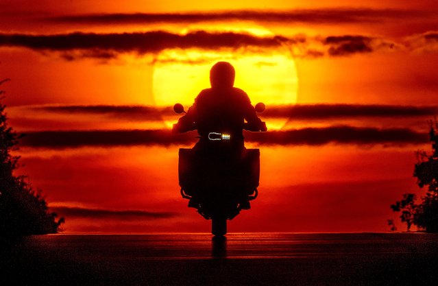 A man rides his bike over a hill as the sun rises in Frankfurt, Germany, Friday, August 9, 2024. (Photo by Michael Probst/AP Photo)