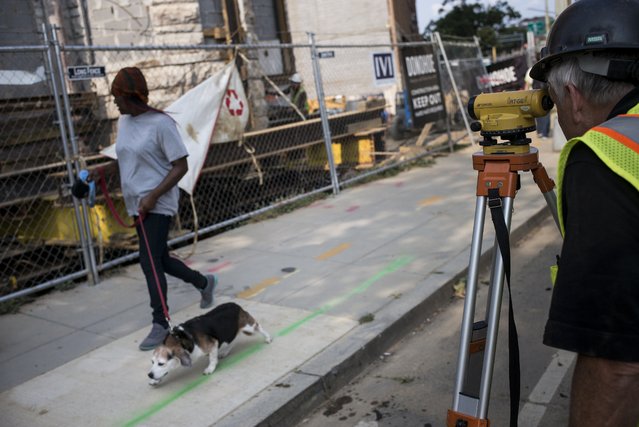 A woman walks a dog past a surveyor as he checks a historic building as it is moved across a lot on New York Avenue July 29, 2014 in Washington, DC.  A team from Expert House Movers have been moving the historic building near L Street in connection with the construction of a new apartment building. (Photo by Brendan Smialowski/AFP Photo)