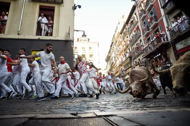 Participants run ahead of bulls during the “encierro” (bull-run) of the San Fermin festival in Pamplona, northern Spain on July 7, 2022. On each day of the festival six bulls are released at 8:00 a.m. (0600 GMT) to run from their corral through the narrow, cobbled streets of the old town over an 850-meter (yard) course. Ahead of them are the runners, who try to stay close to the bulls without falling over or being gored. (Photo by Miguel Riopa/AFP Photo)