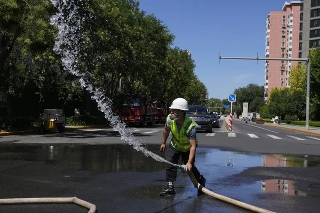 A worker sprays water on a road outside a worksite during a hot day, Thursday, July 14, 2022, in Beijing. A heat wave is sweeping through parts of China. (Photo by Ng Han Guan/AP Photo)