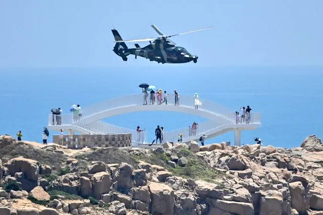 Tourists look on as a Chinese military helicopter flies past Pingtan island, one of mainland China's closest point from Taiwan, in Fujian province on August 4, 2022, ahead of massive military drills off Taiwan following US House Speaker Nancy Pelosi's visit to the self-ruled island. China is due on August 4 to kick off its largest-ever military exercises encircling Taiwan, in a show of force straddling vital international shipping lanes following a visit to the self-ruled island by US House Speaker Nancy Pelosi. (Photo by Hector Retamal/AFP Photo)