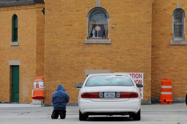 A man prays in the parking lot below icons in the window of the closed adoration chapel at St. Charles Catholic Church amid the coronavirus disease (COVID-19) outbreak in Providence, Rhode Island, U.S., April 23, 2020. (Photo by Brian Snyder/Reuters)