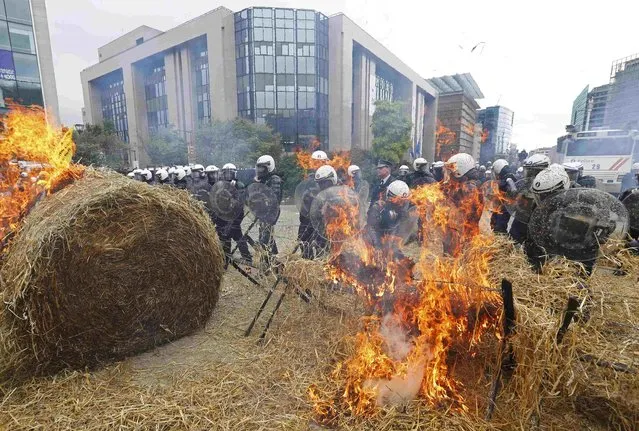 Belgian riot police officers stand guard while demonstrators burn hay as farmers and dairy farmers from all over Europe take part in a demonstration outside an European Union farm ministers emergency meeting at the EU Council headquarters in Brussels, Belgium, September 7, 2015. (Photo by Yves Herman/Reuters)