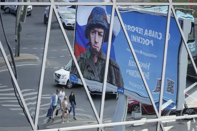 A billboard with a portrait of a Russian soldier and the words “Glory to the heroes of Russia” is reflected in a shopping mall in St. Petersburg, Russia, Saturday, Aug. 20, 2022. (Photo by Dmitri Lovetsky/AP Photo)