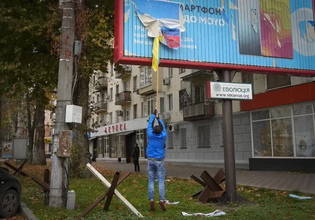A local resident removes the Russian flag from a billboard in central Kherson, Ukraine, Sunday, November 13, 2022. (Photo by Efrem Lukatsky/AP Photo)