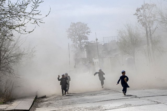 Afghan children run amid a cloud of dust as a military helicopter lands at the green zone area in Kabul on March 23, 2025. (Photo by Wakil Kohsar/AFP Photo)