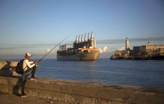 A fisherman holds his rod at the Malecon seawall where the Turkish flagged power ship “Karadeniz Irem Sultan” arrives to Havana Bay in Cuba, Tuesday, November 15, 2022. The ship carrying an electricity plant has arrived to help Cuba meet its demand for electricity. (Photo by Ismael Francisco/AP Photo)