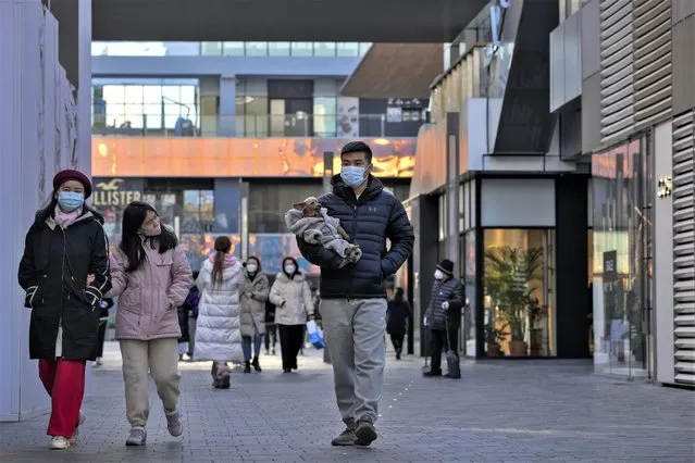 A woman wearing a face mask looks at masked man holding a dog as they walk through a reopened open air shopping mall in Beijing, Sunday, December 4, 2022. China on Sunday reported two additional deaths from COVID-19 as some cities move cautiously to ease anti-pandemic restrictions amid increasingly vocal public frustration over the measures. (Photo by Andy Wong/AP Photo)