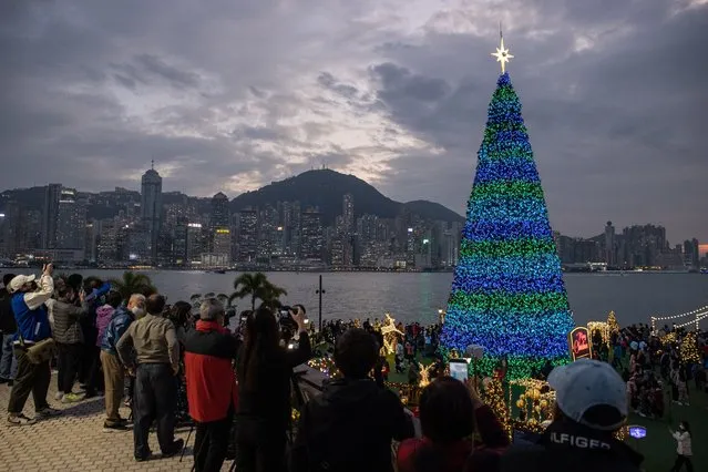 People take photos of a Christmas tree in Hong Kong, China, 12 December 2022. The tree and decorations, set in the West Kowloon Cultural District and Victoria Harbour, are part of the Hong Kong WinterFest Christmas Town 2022. (Photo by Jerome Favre/EPA/EFE)