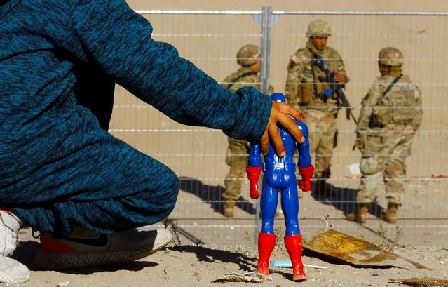 George, 5, a migrant boy from Venezuela who is traveling with his family and trying to seek asylum in the United States, plays with a Captain America doll at the border between Mexico and the United States, while members of the Texas National Guard stand guard on the banks of the Rio Bravo river, with the purpose of reinforcing border security and inhibiting the crossing of migrants to the United States, seen from Ciudad Juarez, Mexico on December 27, 2022. (Photo by Jose Luis Gonzalez/Reuters)