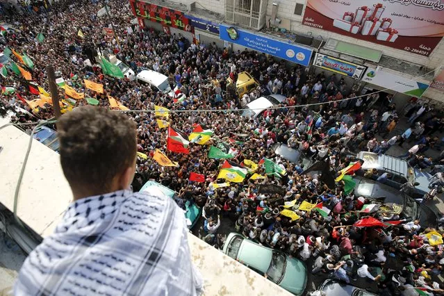 A Palestinian watches as mourners take part in the funeral of Palestinian Mohnad Halabi, who was killed after stabbing and killing an off-duty Israeli soldier and a rabbi in Jerusalem's Old City on Saturday, near the West Bank city of Ramallah October 9, 2015. (Photo by Mohamad Torokman/Reuters)