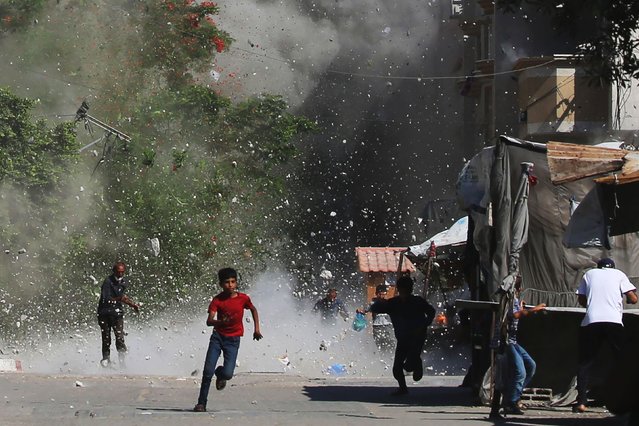 Palestinians rush for cover as debris flies around them after an Israeli strike on the Bureij camp for Palestinian refugees in the central Gaza Strip on June 15, 2025. Gaza's civil defence agency said 16 people were killed in Israeli military operations in the Palestinian territory on June 15, most of them while waiting for aid. (Photo by Eyad Baba/AFP Photo)