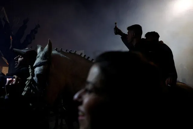 A rider holds a beer during the annual “Luminarias” celebration on the eve of Saint Anthony's day, Spain's patron saint of animals, in the village of San Bartolome de Pinares, northwest of Madrid, Spain on January 16, 2023. (Photo by Susana Vera/Reuters)