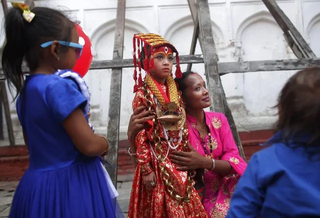 A Nepalese woman gets photographed with a young girl dressed as the Living Goddess Kumari while waiting for the Kumari puja to start at Hanuman Dhoka temple, in Kathmandu, Nepal, Wednesday, September 14, 2016. Girls under the age of nine gathered for the Kumari puja, a tradition of worshiping young prepubescent girls as manifestations of the divine female energy. The ritual holds a strong religious significance in the Newar community that seeks divine blessings to save small girls from diseases and bad luck in the years to come. (Photo by Niranjan Shrestha/AP Photo)