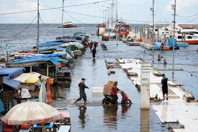 A motorcyclist carries boxes through water at Kali Adem port, which is impacted by high tides due to the rising sea level and land subsidence, north of Jakarta, Indonesia on November 20, 2020. (Photo by Willy Kurniawan/Reuters)