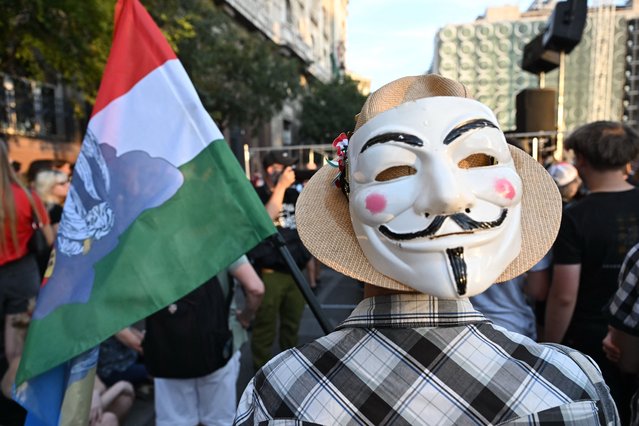 A demonstrator holds a Hungarian flag and a Guy Fawkes mask as teachers, students and their sympathizers protest in central Budapest at the headquarters of the Interior Ministry on September 2, 2024, after the head of the renowned Madach Imre high school was sacked last week for not implementing a government-mandated “smartphone ban”. In August, schools were instructed to collect students' phones and smart devices during the teaching hours in a decree signed by nationalist Prime Minister Viktor Orban. The principal of the Madach Imre High School was fired, after it refused to implement the ban, citing a part of the regulation. (Photo by Attila Kisbenedek/AFP Photo)
