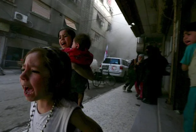 Ghazal, 4, (L) and Judy, 7, carrying 8-month-old Suhair, run away after the shelling of a Red Crescent convoy in Damascus, Syria May 6, 2015. Bassam Khabieh: I was covering the Syrian Arab Red Crescent convoy's visit to the the Douma neighborhood of Damascus, which was carrying medical aid and supplies used to give psychological support to children affected by war. (Photo by Bassam Khabieh/Reuters)