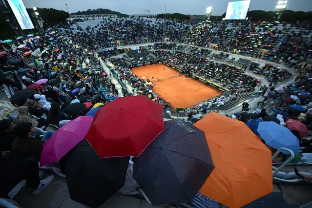 Spectators in the Central Court protect temselves as the rain interrupts the third round of the Men's ATP Rome Open tennis tournament between Greece's Stefanos Tsitsipas and Italy's Lorenzo Sonego at Foro Italico in Rome on May 15, 2023. (Photo by Filippo Monteforte/AFP Photo)