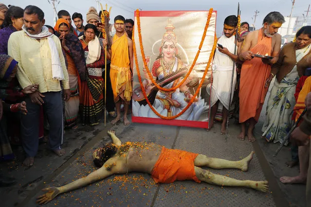 A Hindu Holy man lies in front of an image of Hindu Goddess of learning Saraswati, at Sangam, the sacred confluence of the rivers Ganga, Yamuna and the mythical Saraswati, during Magh Mela festival, in Prayagraj, India. Tuesday, February 16, 2021. Hindus believe that ritual bathing on auspicious days can cleanse them of all sins. A tented city for the religious leaders and the believers has come up at the sprawling festival site with mounted police personnel keeping a close watch on the activities. The festival is being held amid rising COVID-19 cases in some parts of India after months of a steady nationwide decline. (Photo by Rajesh Kumar Singh/AP Photo)