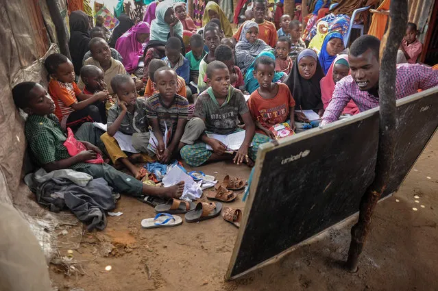 University student Yahye Mohamed (R) teaches alphabets and numbers to displaced Somali children and teenagers as a volunteer teacher at a makeshift school at the Badbado IDP camp in Mogadishu, Somalia, on June 25, 2018. University students from various universities provide voluntarily free schooling to about 600 girls and boys under 16- year- old at various IDP camps in Mogadishu since May 2017. (Photo by Mohamed Abdiwahab/AFP Photo)