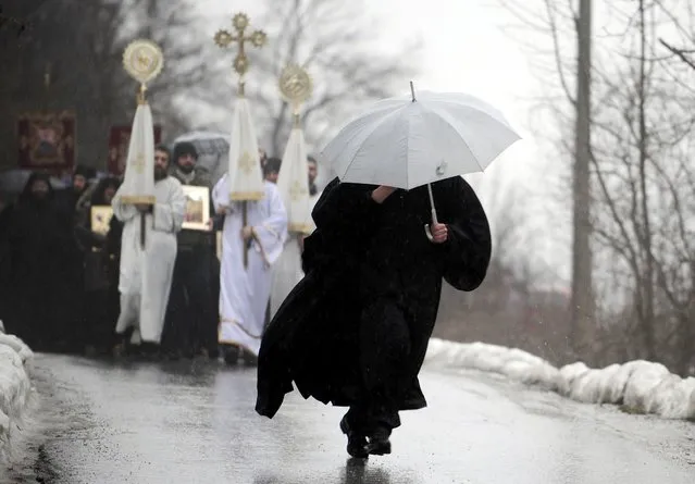 A priest, carrying an umbrella, heads a procession during an Epiphany day celebration in Bitushe village, about 150km (93 miles) west from the capital Skopje, January 19, 2015. Bitushe practises a different Epiphany tradition. (Photo by Ognen Teolovski/Reuters)