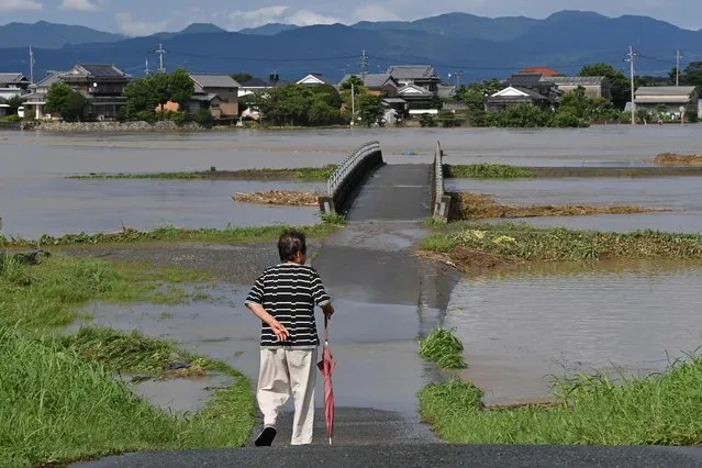 A woman looks out over an area covered in water from a swollen river in the town of Tachiarai, Fukuoka prefecture, on July 10, 2023, after heavy rains hit wide areas of Kyushu island. One person died in a landslide and hundreds of thousands of people have been urged to evacuate their homes in southwestern Japan as forecasters on July 10 warned of the “heaviest rain ever” in the region. (Photo by Kazuhiro Nogi/AFP Photo)