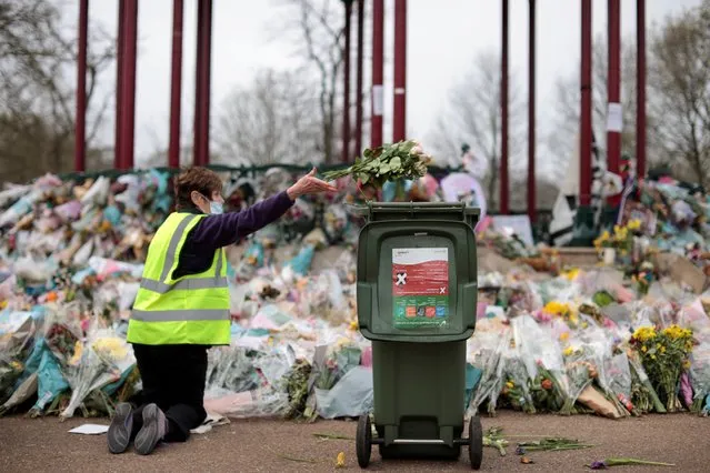 A member of Clapham Women's Institute clears floral tributes from a makeshift memorial for murdered woman Sarah Everard from the Clapham Common Bandstand in London, Britain, April 1, 2021. London police acted appropriately at a vigil for the woman earlier this month, an independent watchdog said, after the force was criticised for a heavy-handed approach which saw mourners dragged away by officers. (Photo by Hannah McKay/Reuters)