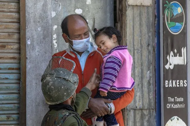 An Indian paramilitary soldier plays with a Kashmiri child during a gunbattle between Indian soldiers and suspected militants in Shopian, south of Srinagar, Indian controlled Kashmir, Friday, April 9, 2021. Seven suspected militants were killed and four soldiers wounded in two separate gunfights in Indian-controlled Kashmir, officials said Friday, triggering anti-India protests and clashes in the disputed region. (Photo by Dar Yasin/AP Photo)