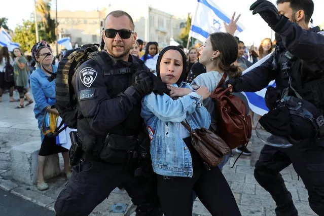 An Israeli policeman removes a Palestinian woman from the area as youth from far-right Israeli groups participate in a flag-waving procession at Damascus Gate, just outside Jerusalem's Old City on June 15, 2021. (Photo by Ammar Awad/Reuters)