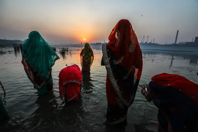 Indian Hindu devotees worship the setting sun while celebrating Chhath Puja at Sabarmati river in Ahmedabad, India, 13 November 2018. “Chhath Puja” is a worship of the setting and rising sun and is dedicated to Chhatti Mai (Goddess of Power). The festival is seen as a serene event when bejewelled women in colourful saris visit the banks of rivers and ponds, singing folk songs. They then take a dip in the water and pray to the sun god. (Photo by Divyakant Solanki/EPA/EFE)