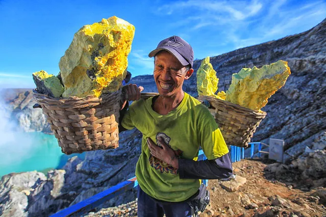 A miner in East Java, Indonesia, carries sulphur in reed baskets that weigh up to 90kgs. Twice a day he climb two miles (3km) up the mountain, then heads downward more than 200 metres into the Ijen volcano, where the sulphur crystals form. He works without any protection in stifling heat and breathing sulphurous gas that burns his lungs. (Photo by Tadeja Horvat/The Guardian)
